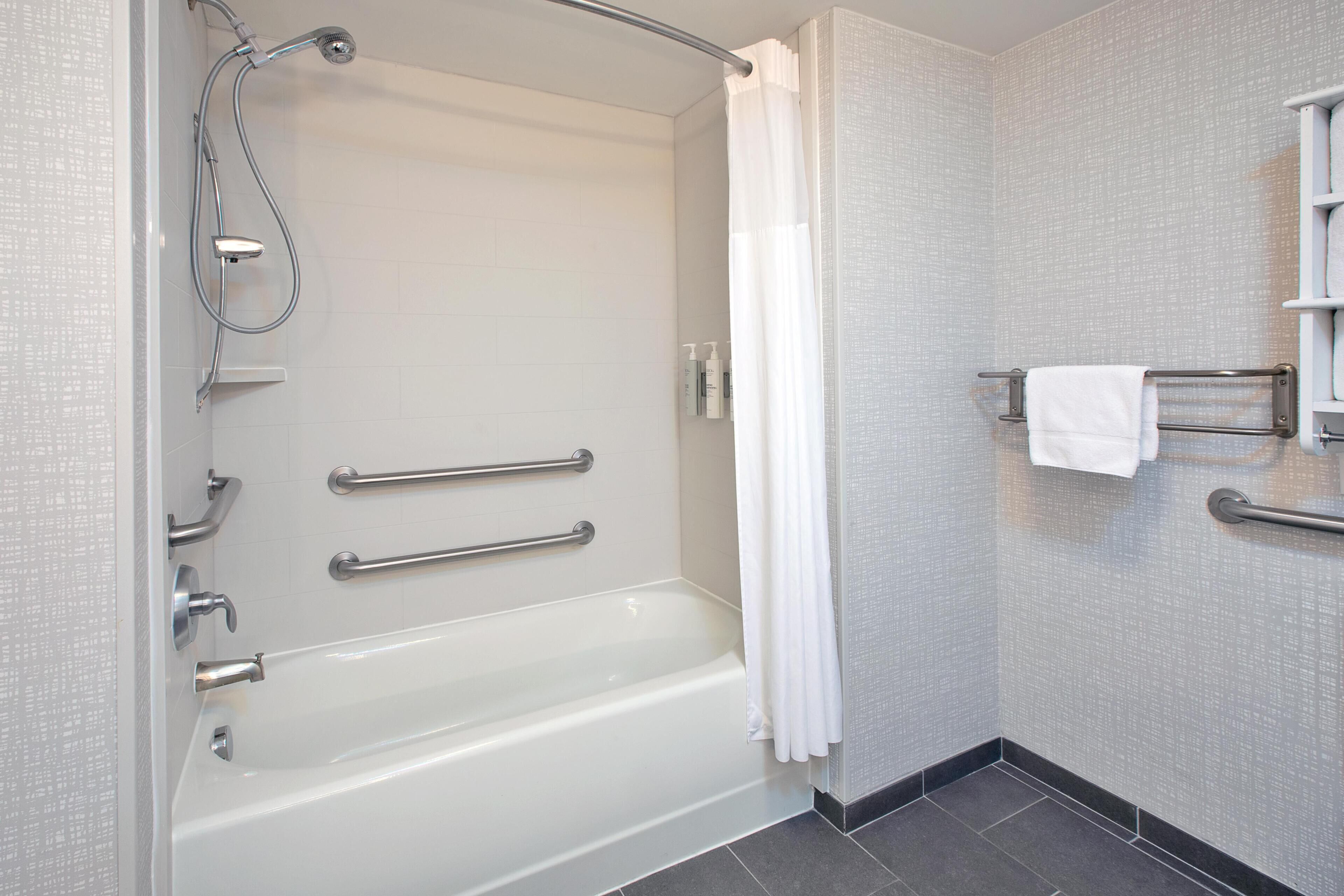 A modern bathroom with a bathtub, grab bars, a shower, and a towel rack.