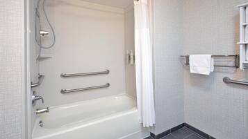 A modern bathroom with a bathtub, grab bars, a shower, and a towel rack.