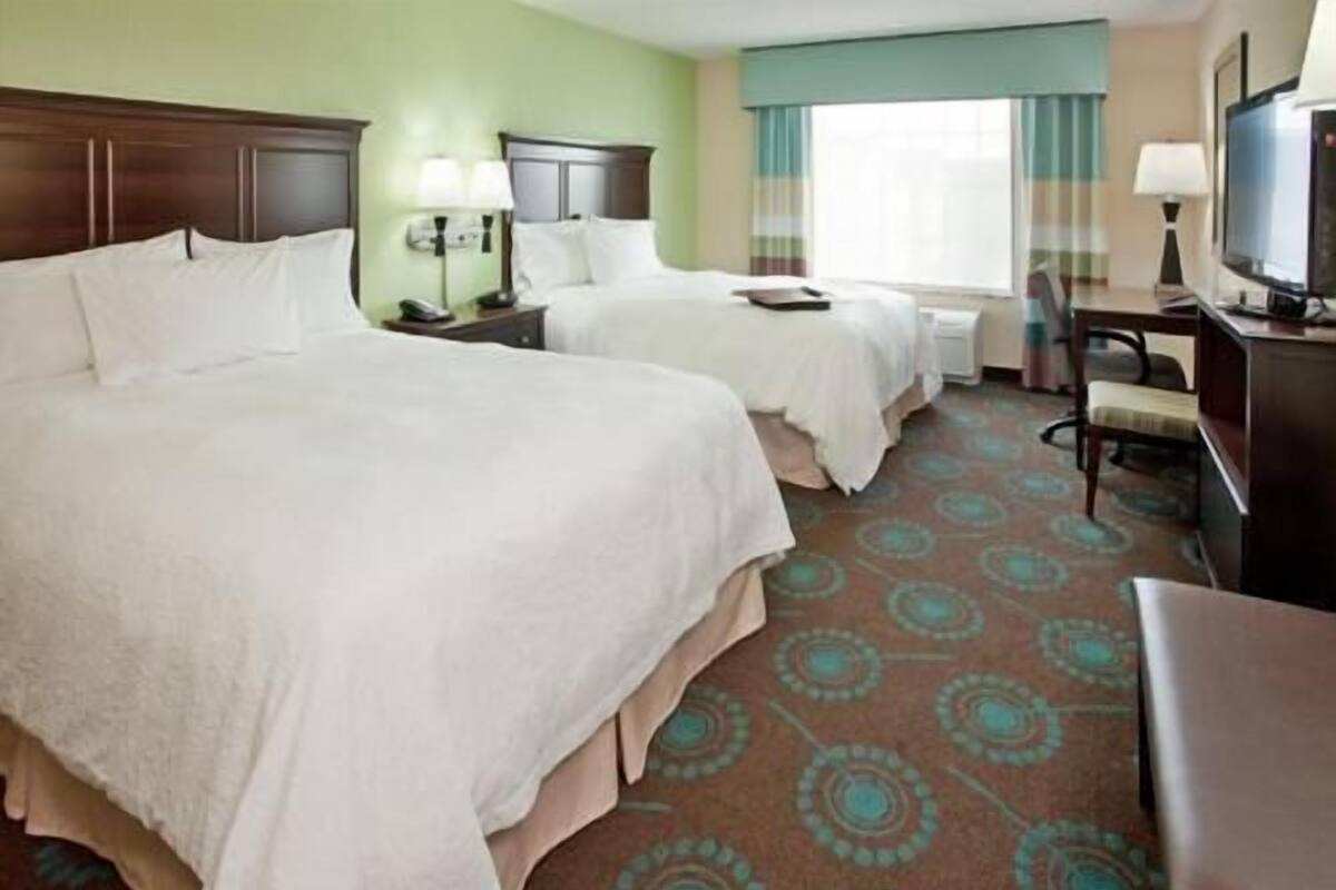 A hotel room with two beds, a desk, a television, and a window with curtains.
