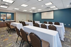A conference room with rows of tables and chairs, a projector screen, and a coffee station.