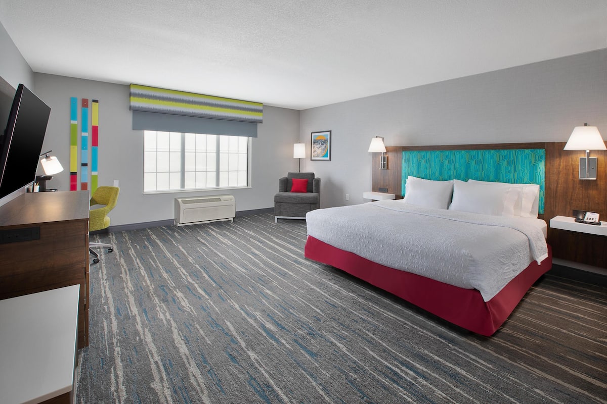 A hotel room with a bed, a desk, a chair, a TV, and a window.