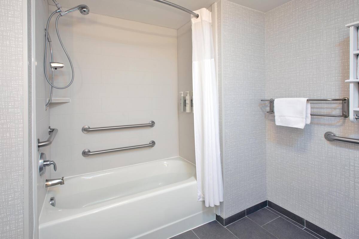A modern bathroom with a bathtub, shower, grab bars, and a towel rack.