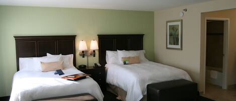 A hotel room with two beds, a nightstand with lamps, a bench, and a painting on the wall.