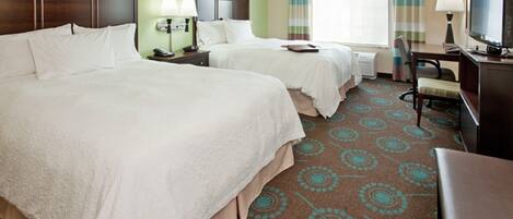 A hotel room with two beds, a desk, a chair, a television, and a window with curtains.