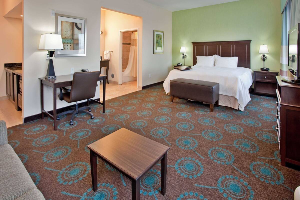 A hotel room with a bed, desk, chair, and a small table.