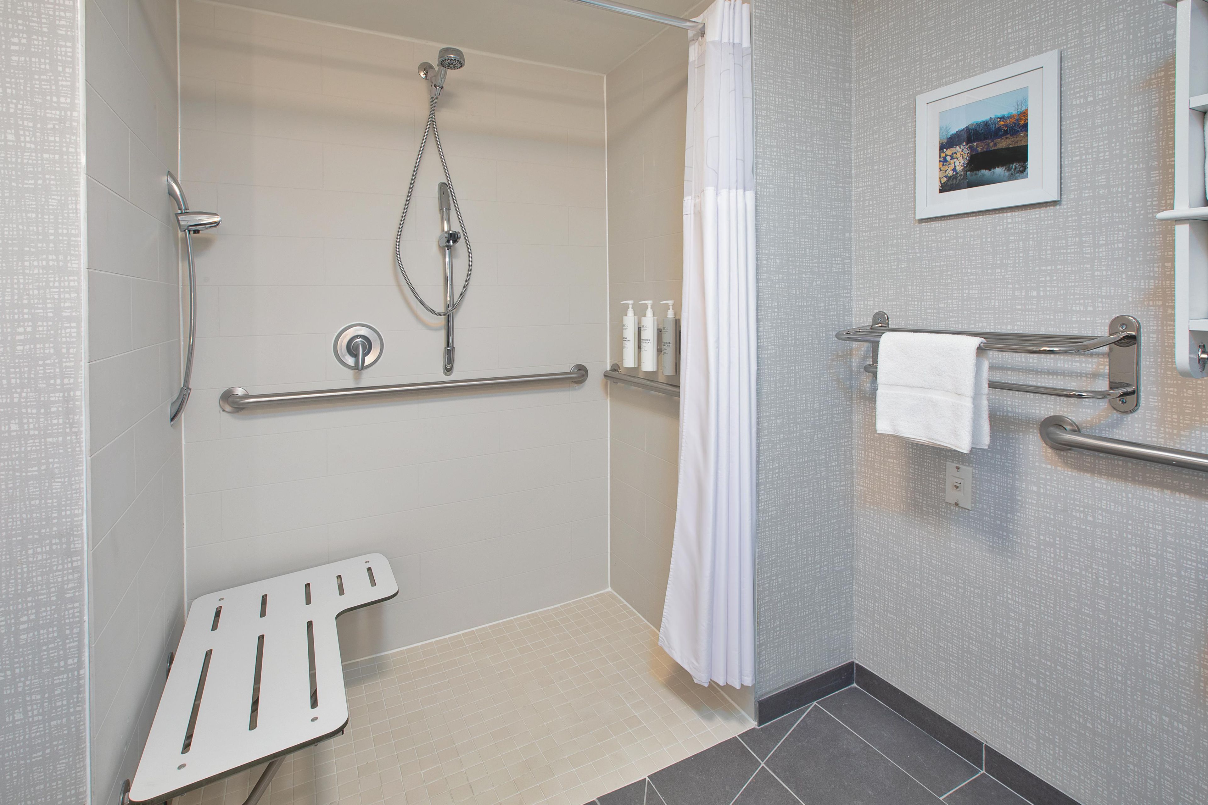 A bathroom with a shower, grab bars, a towel rack, and a picture on the wall.