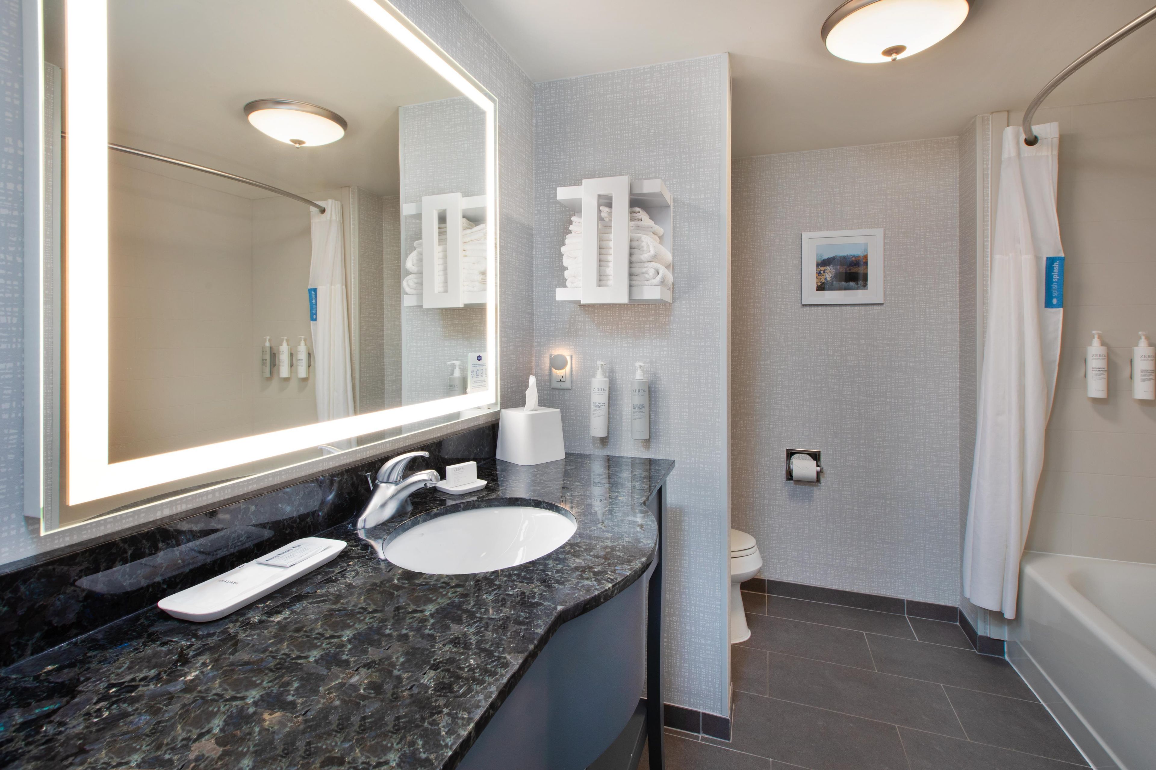 A bathroom with a large mirror, a sink, a toilet, and a shower area.