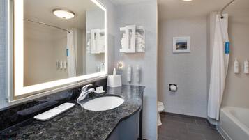 A bathroom with a large mirror, a sink, a toilet, and a shower area.