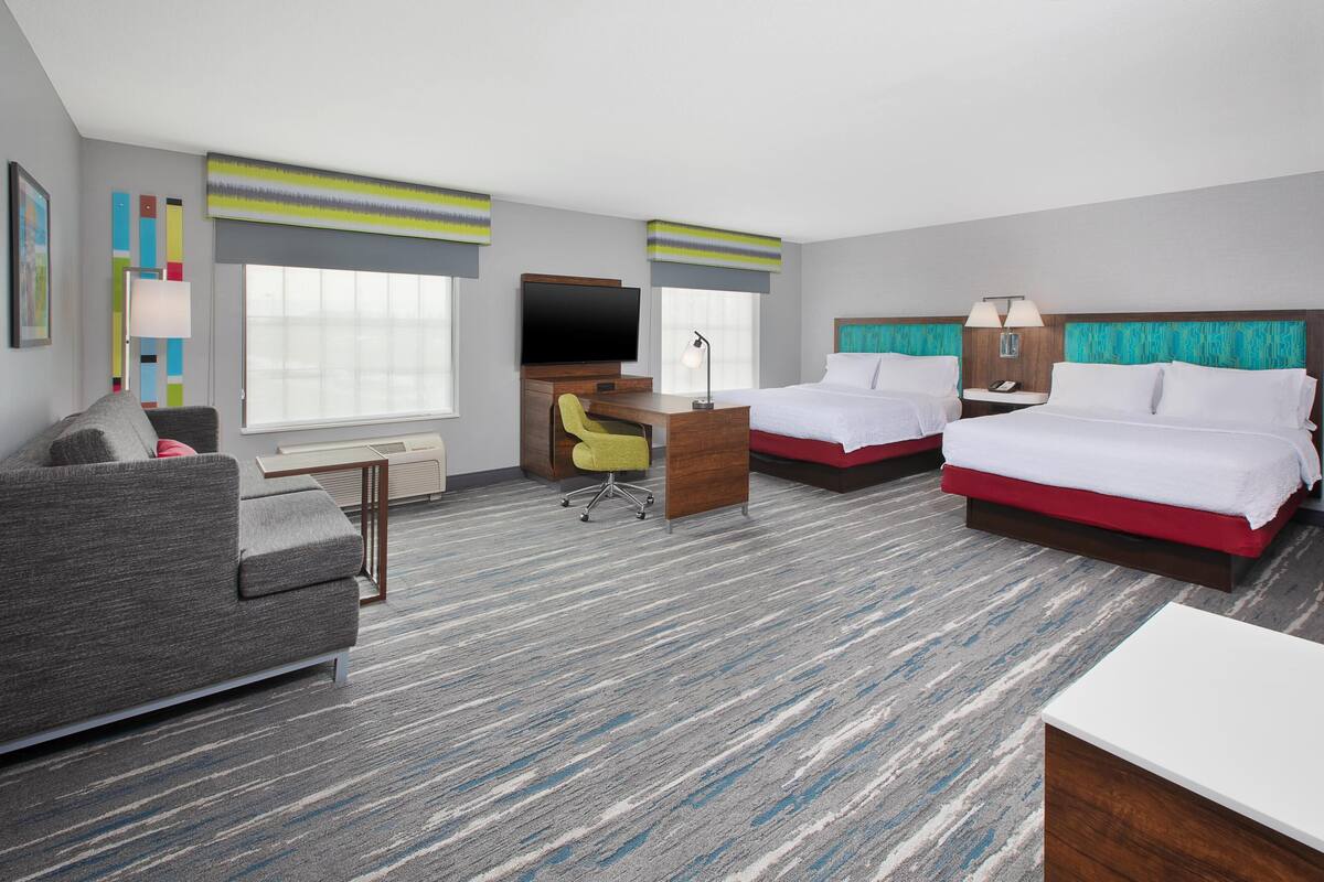 A hotel room with two beds, a desk, a TV, a sofa, and a chair.