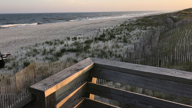 Una terraza de madera con vistas a una playa con dunas y una valla de madera.