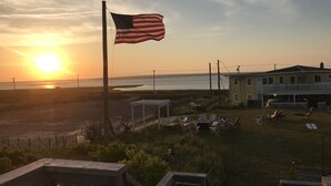 Vista al atardecer con una bandera estadounidense, una playa y un edificio con terraza.