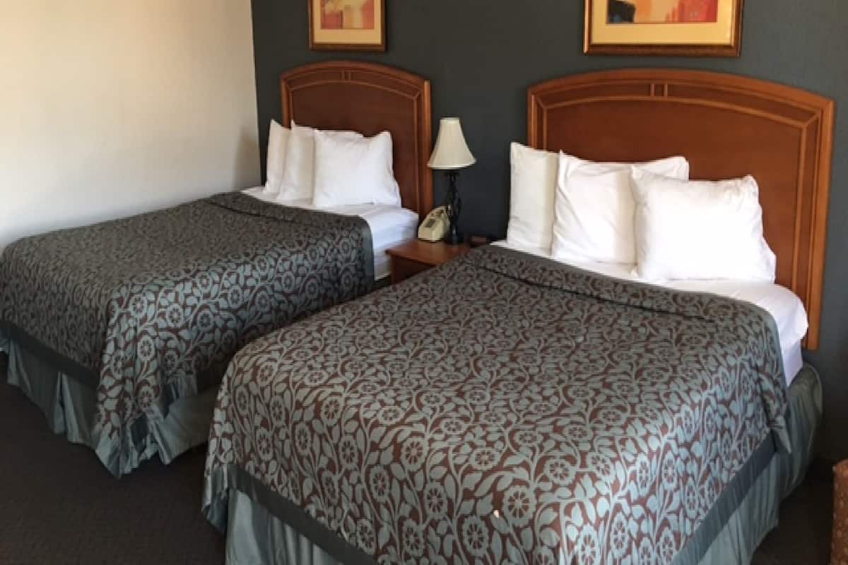 Ett hotellrum med två sängar, var och en med ett mönstrat överkast och vita kuddar. På väggarna hänger två tavlor, och det finns ett nattduksbord med en lampa och en telefon.