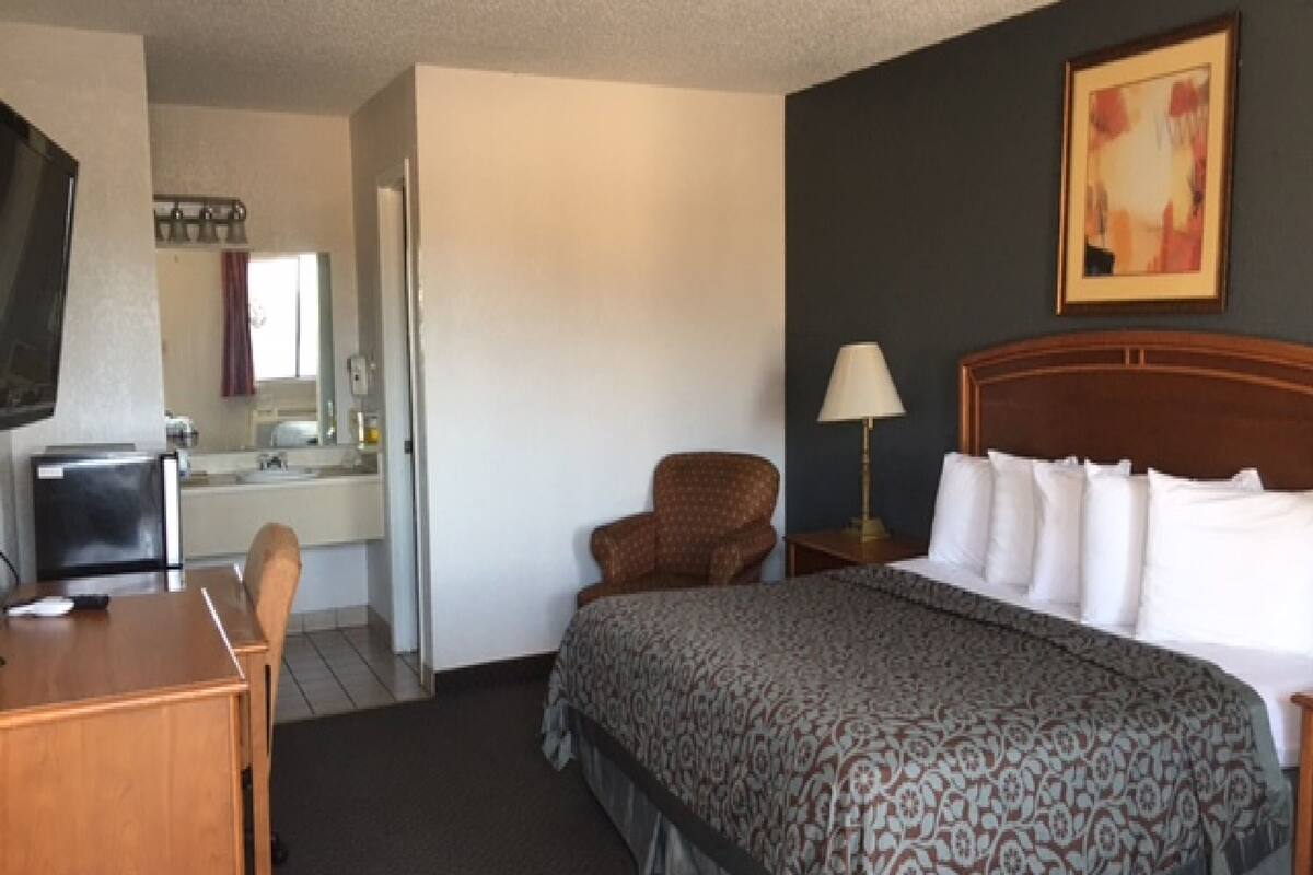 Ett hotellrum med en säng, ett skrivbord med en stol, en tv, en lampa och en tavla på väggen.
