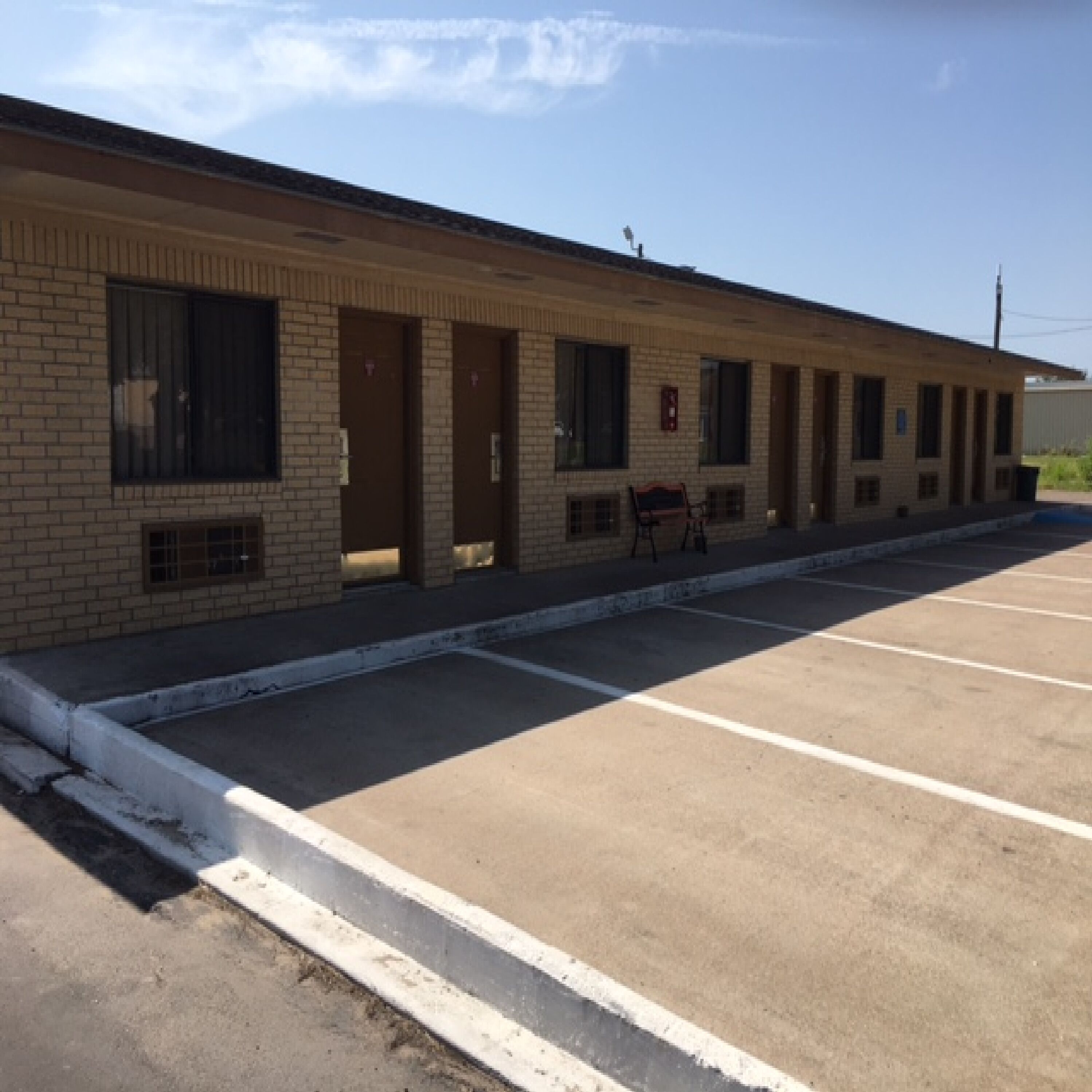 A motel with a long, single-story brick facade, multiple doors, and a parking lot.