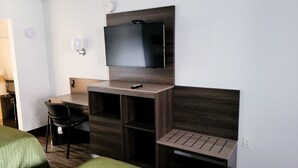 Ein Hotelzimmer mit einem Bett, einem Schreibtisch mit Stuhl, einem an der Wand befestigten Fernseher und einem kleinen Tisch.
