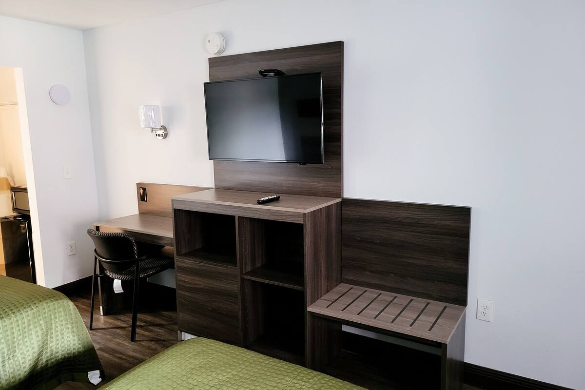 A hotel room with a bed, a desk with a chair, a television mounted on the wall, and a small table.