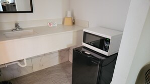 Eine kompakte Küchenzeile mit einem weißen Spülbecken, einer Mikrowelle und einem schwarzen Kühlschrank.