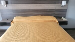 Ein Bett mit einer gelben, strukturierten Decke, einem hölzernen Kopfteil sowie Nachttischen mit Lampen und einem Telefon.