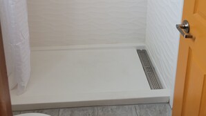 Ein Duschbereich mit weißer Wand mit Struktur, einer Duschvorhang, einem Metallgriff und einer Tür mit Griff.