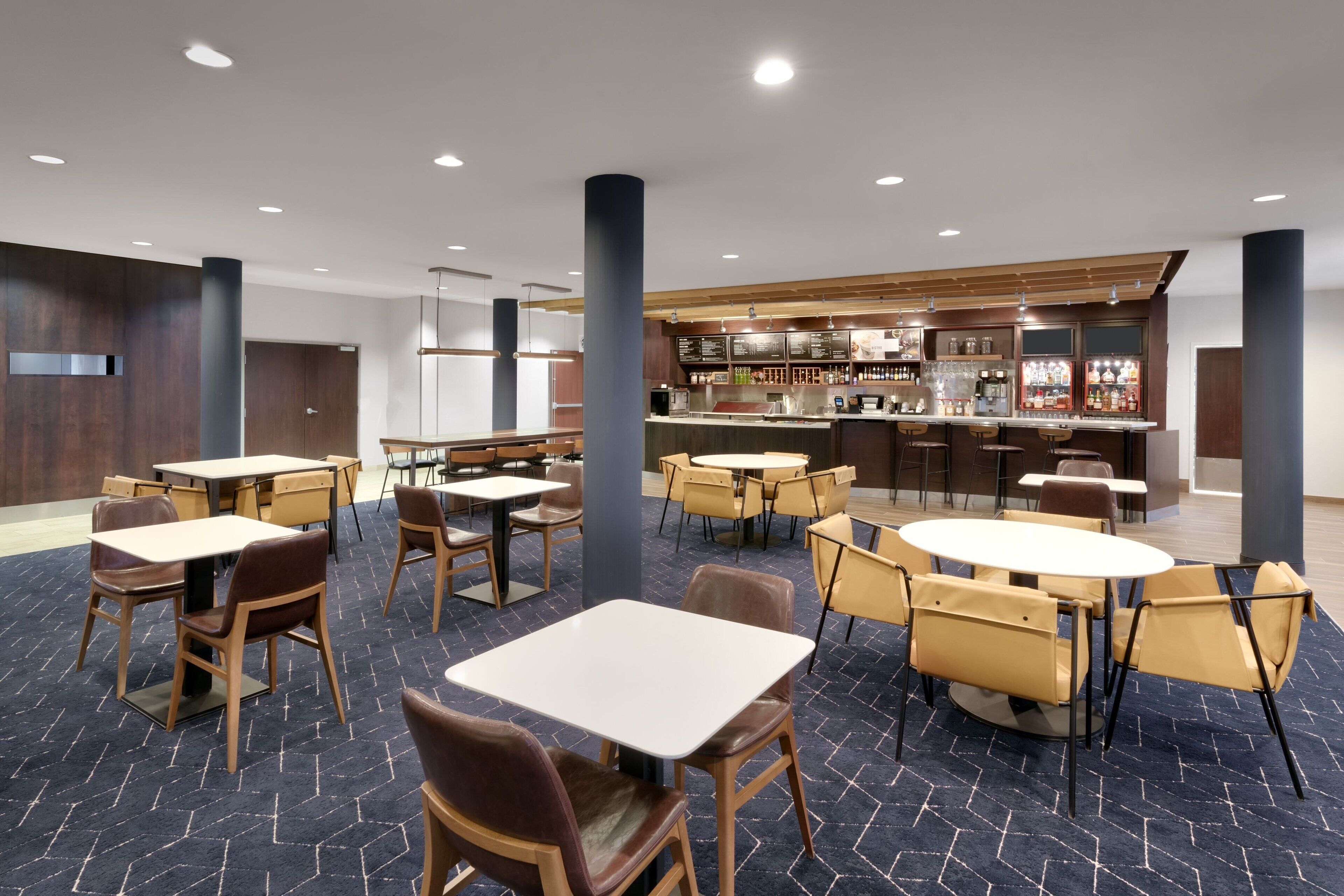 En moderne hotellobby med flere spiseborde og stole, et barområde og en reception.