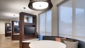 Un salon moderne avec un téléviseur à écran plat, une table ronde et un canapé en cuir noir agrémenté de coussins.