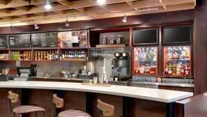 Un espace bar avec des tabourets, un tableau affichant le menu et des étagères remplies de bouteilles et de verres.