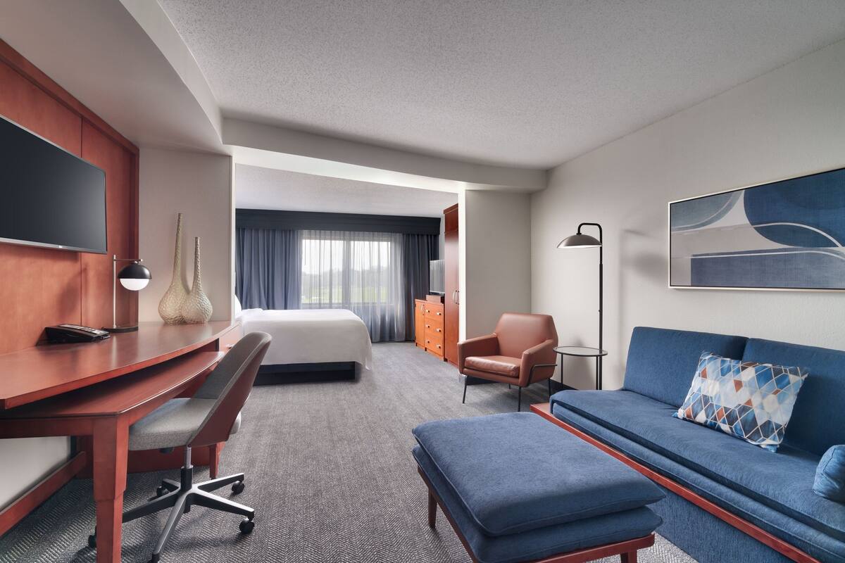 Ein Hotelzimmer mit Bett, Schreibtisch, Sofa, Sessel und Fernseher.