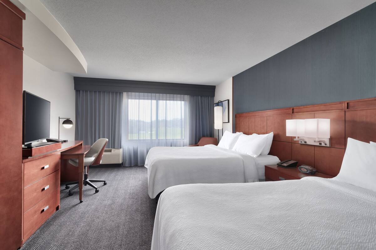 Ein Hotelzimmer mit zwei Betten, einem Schreibtisch, einem Sessel, einem Schminktisch und einem Fernseher.