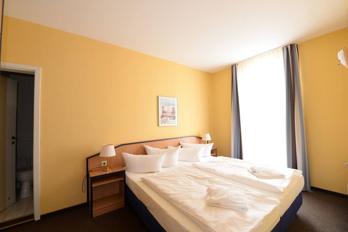 Habitación de hotel con cama, mesitas de noche, cortinas y puerta.
