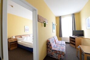 Una camera d'albergo con un letto, una poltrona, una scrivania, una televisione e una finestra con tende.