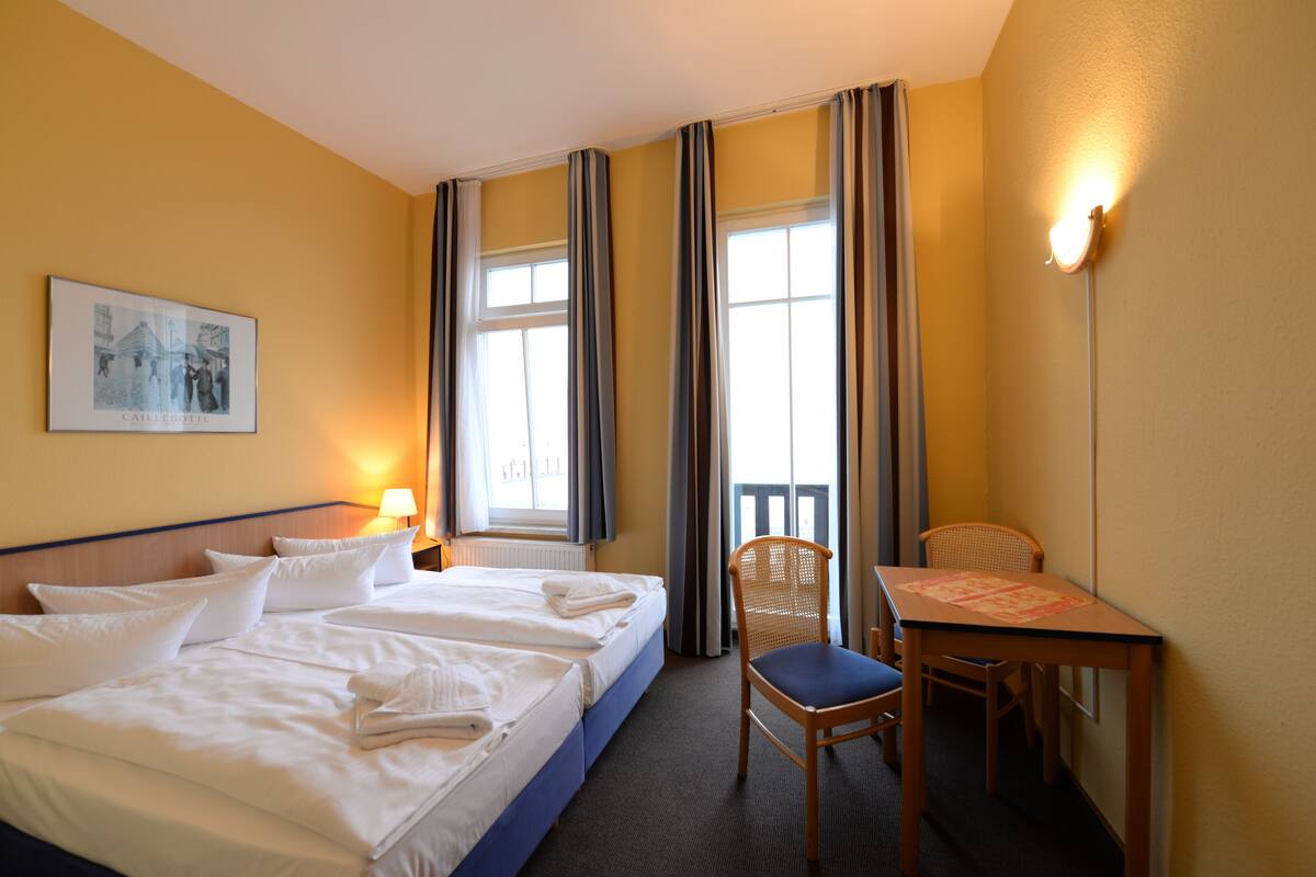 Habitación de hotel con cama, escritorio, silla, lámpara y ventana con cortinas.