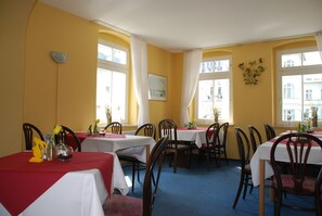 Zona pranzo con tavoli apparecchiati per due, sedie e una parete gialla.