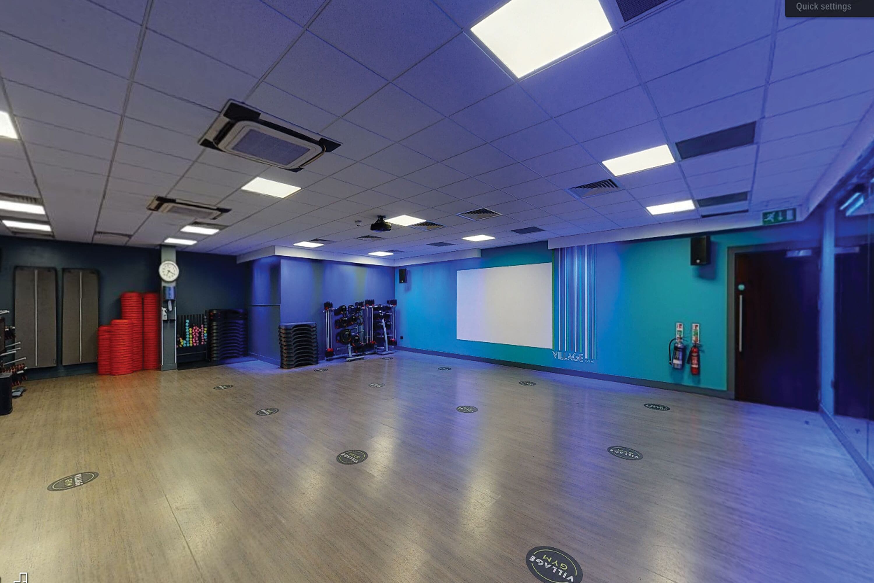 A spacious room with a wooden floor, ceiling lights, a projector screen, and exercise equipment.