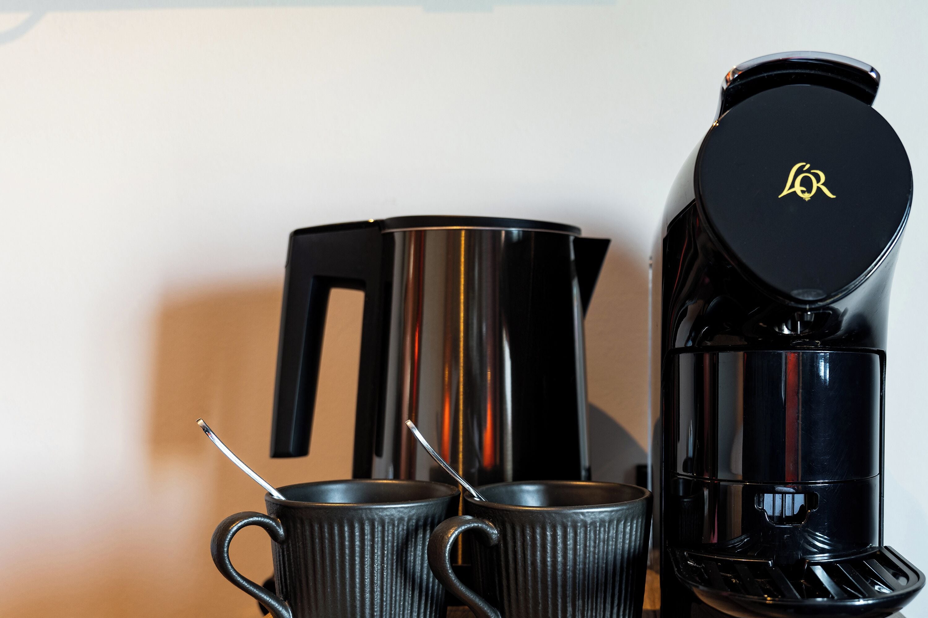 A coffee maker, two mugs, and a kettle on a table.