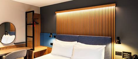Ein modernes Hotelzimmer mit einem großen Bett, einem Schreibtisch mit Stuhl, einem Nachttisch mit Lampe und einem Spiegel.