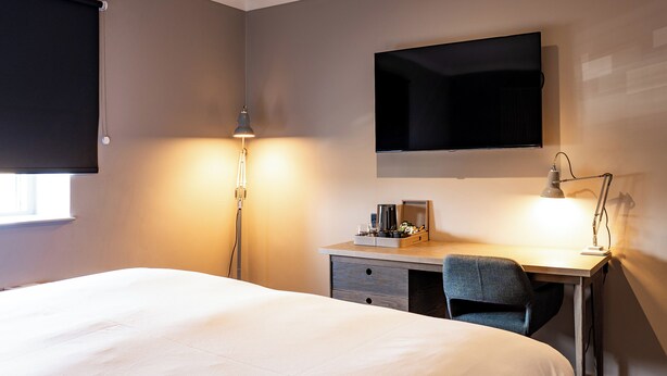 A hotel room with a bed, desk, chair, lamp, and a flat-screen TV mounted on the wall. - Village Hotel Solihull (Solihull)