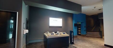 A reception area with a dark reception desk, a digital display, and a staircase in the background.