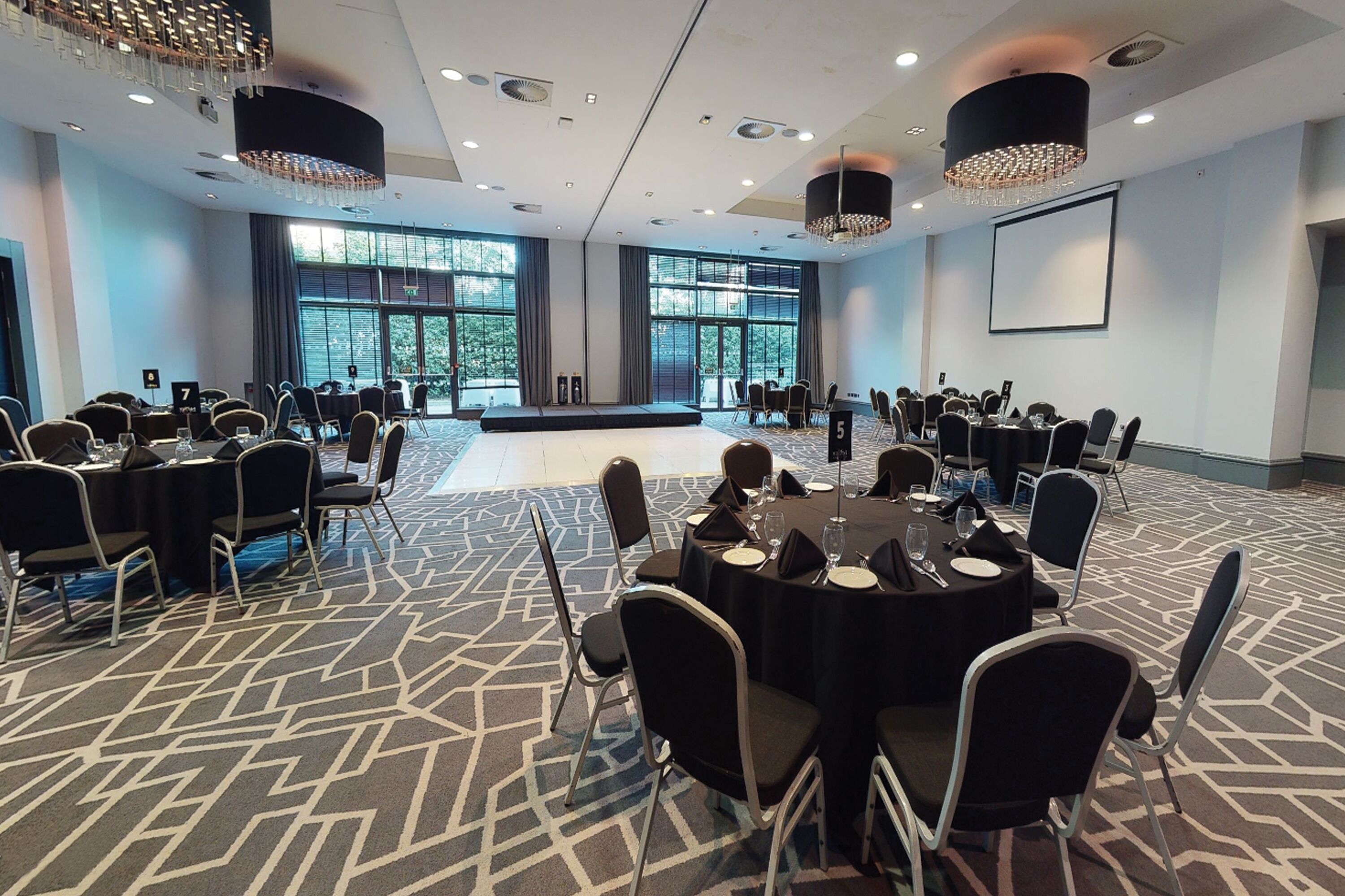 A conference room with multiple tables and chairs, large windows, and a stage.