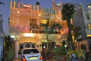 Um hotel com uma placa indicando "HOTEL" e "HOTEL BANGKOK". Há um carro estacionado na frente, e o edifício está decorado com luzes de Natal.