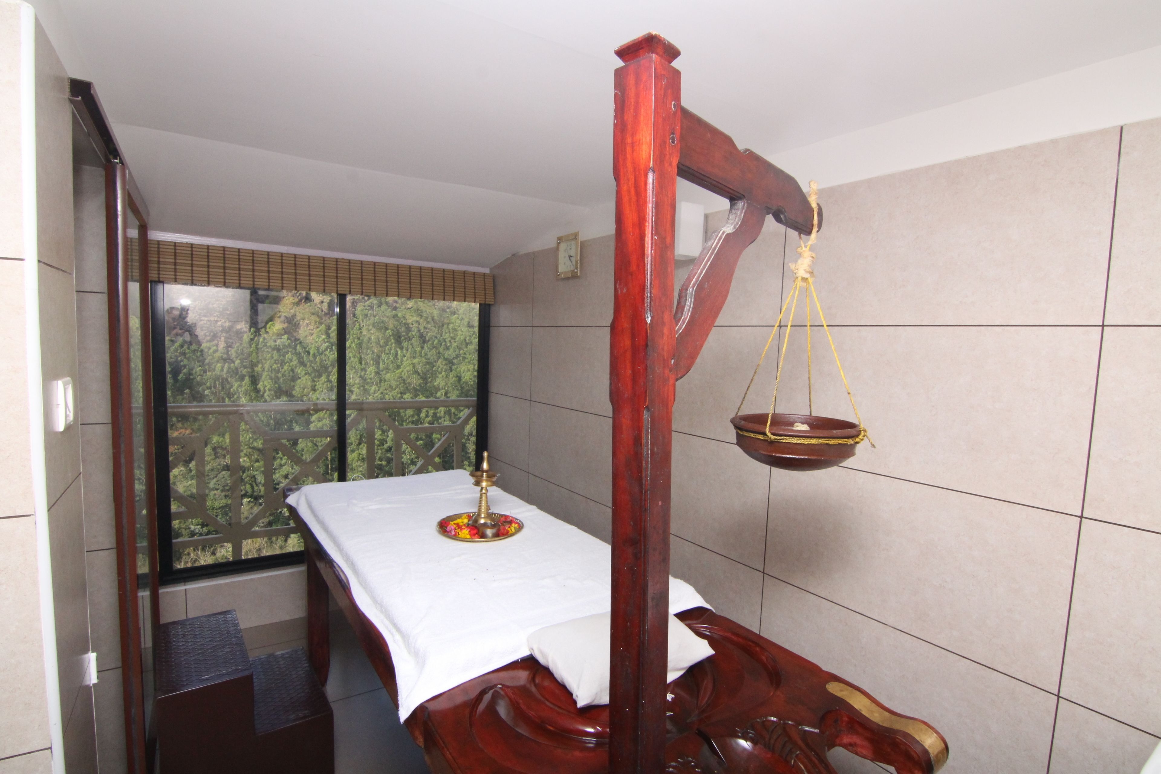 A room with a bed, a window with a view of greenery, and a traditional scale.