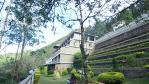 A landscaped garden with a building featuring a balcony, surrounded by well-maintained hedges and trees. - Abad Copper Castle (Devikolam)