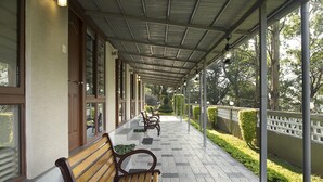 A covered walkway with benches, glass doors, and a view of greenery. - Abad Copper Castle (Devikolam)