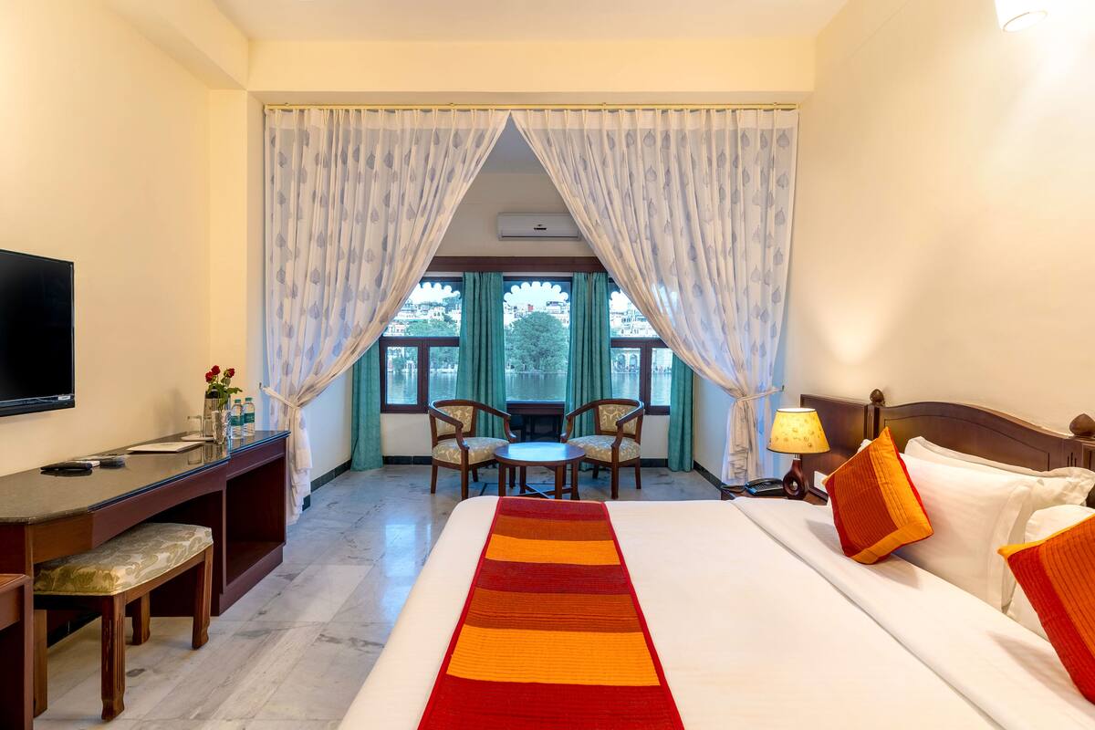 Habitación de hotel con una cama grande, un escritorio con silla, televisión y vista al exterior a través de una ventana con cortinas.