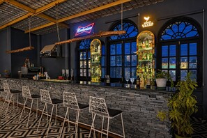 A bar area with a stone wall, bar stools, and a Budweiser sign. - Hotel Sarovar on Lake Pichola (Udaipur)