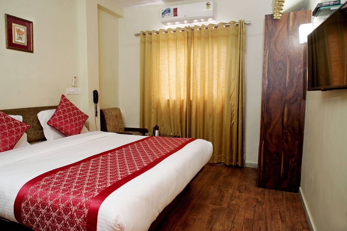 Habitación de hotel con una cama grande, un armario de madera, un teléfono y una ventana con cortinas.