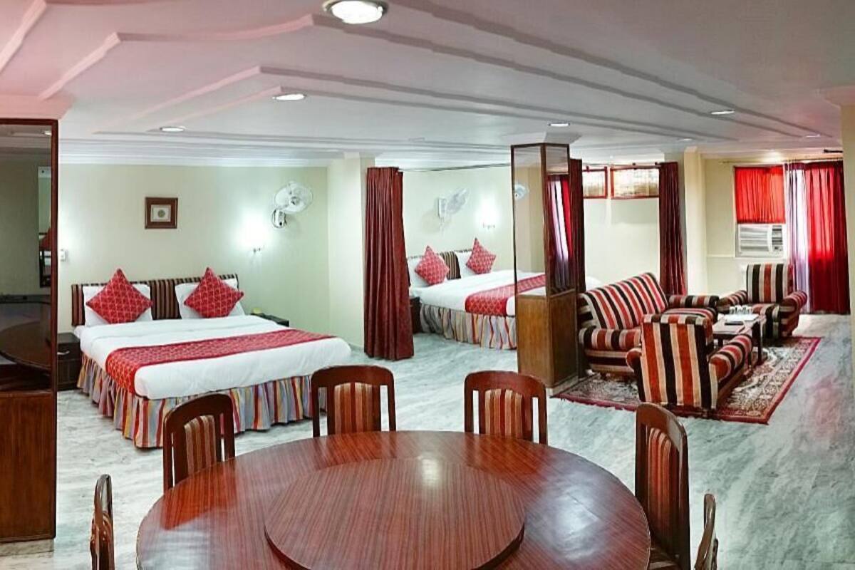 Una habitación de hotel con una cama grande, una cama más pequeña, una mesa de comedor con sillas y un conjunto de sofás.