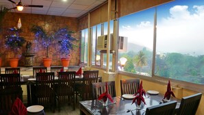 Un ristorante con tavoli apparecchiati, ampie finestre vista su aree verdi e piante ornamentali.