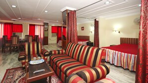 Camera d'albergo con un divano a righe, un'area pranzo con sedie, un letto con copriletto rosso e pavimento rivestito di moquette.