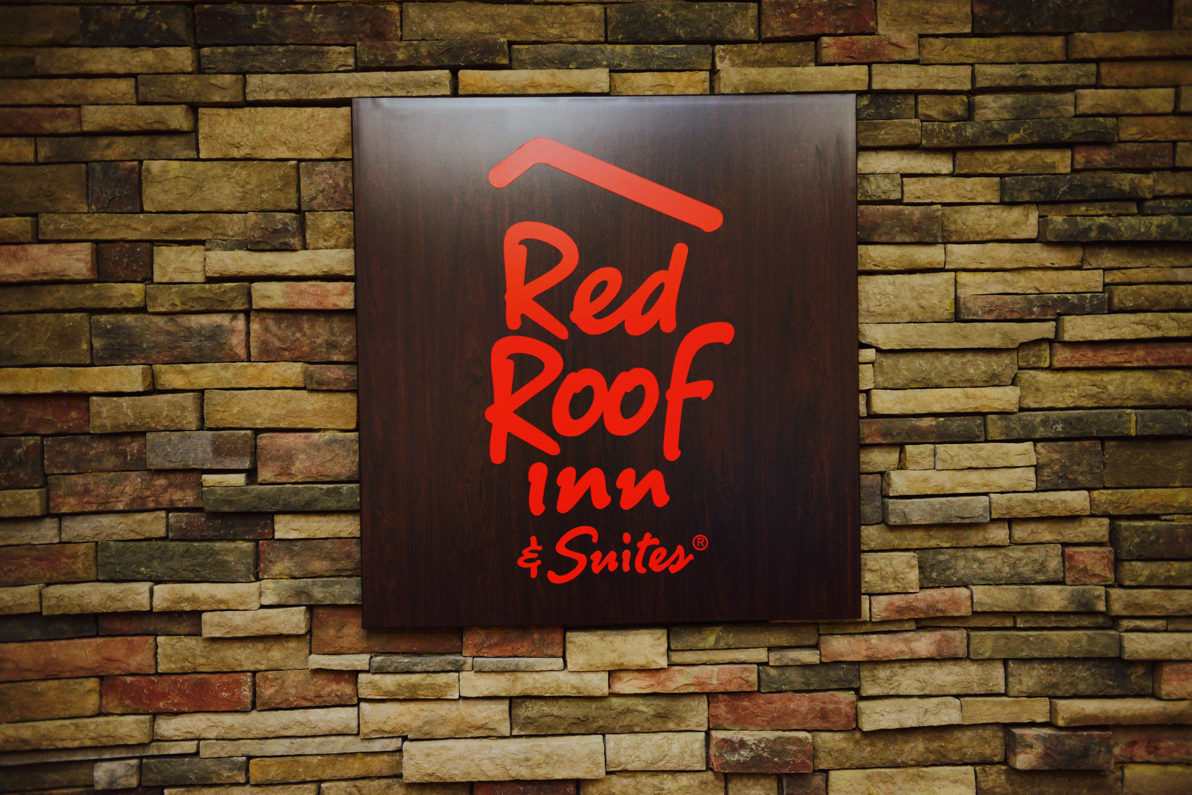 A sign for Red Roof Inn & Suites against a stone wall backdrop.