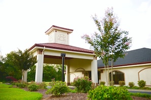 A building with a covered entrance, a tower with a clock, and a garden with various plants.